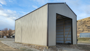 A 24x36x16 Commercial Feed Truck Storage pole barn, built by MQS, featuring taupe metal siding, and dark brown metal trim and roofing, in Norris, MT