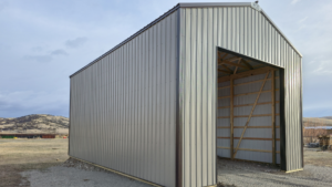 A 24x36x16 Commercial Feed Truck Storage pole barn, featuring taupe metal siding, and dark brown metal trim and roofing, built by MQS, in Norris, MT